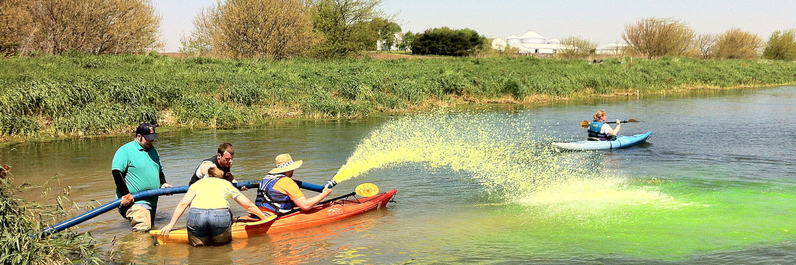 Students on a boat spraying green foam on the lake for water center research.